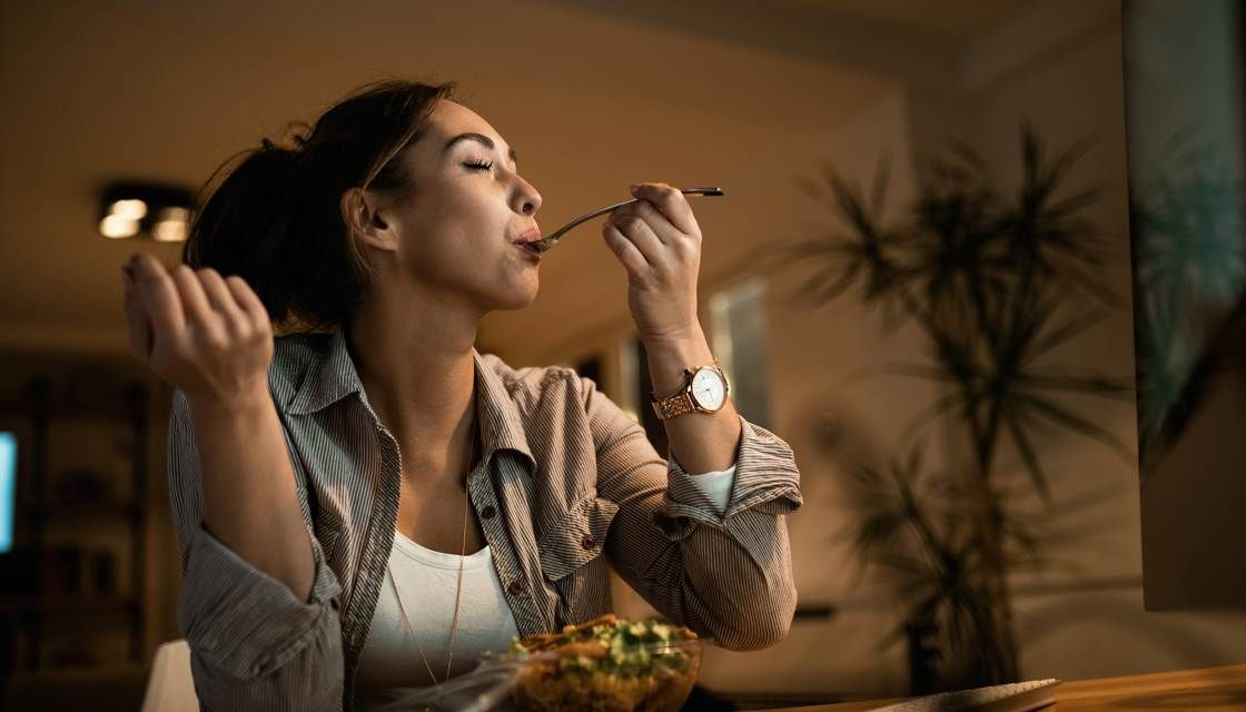 Mujer comiendo sola de noche como ejemplo de impulso alimentario y pérdida de control de impulsos hacia la comida